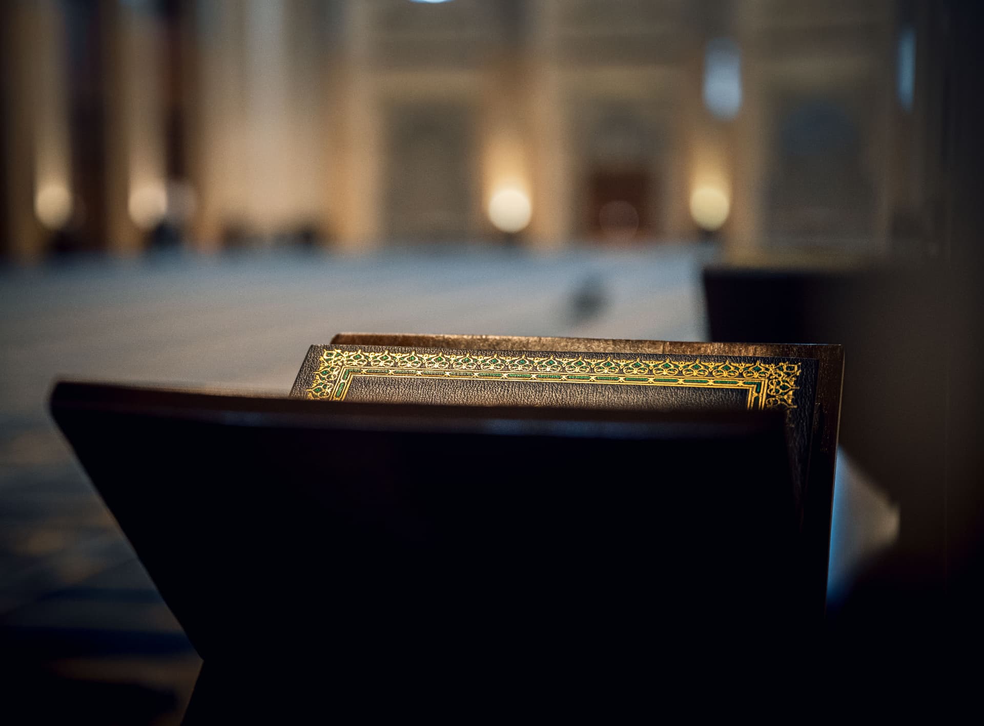 A Quran resting on a wooden stand inside a softly lit mosque